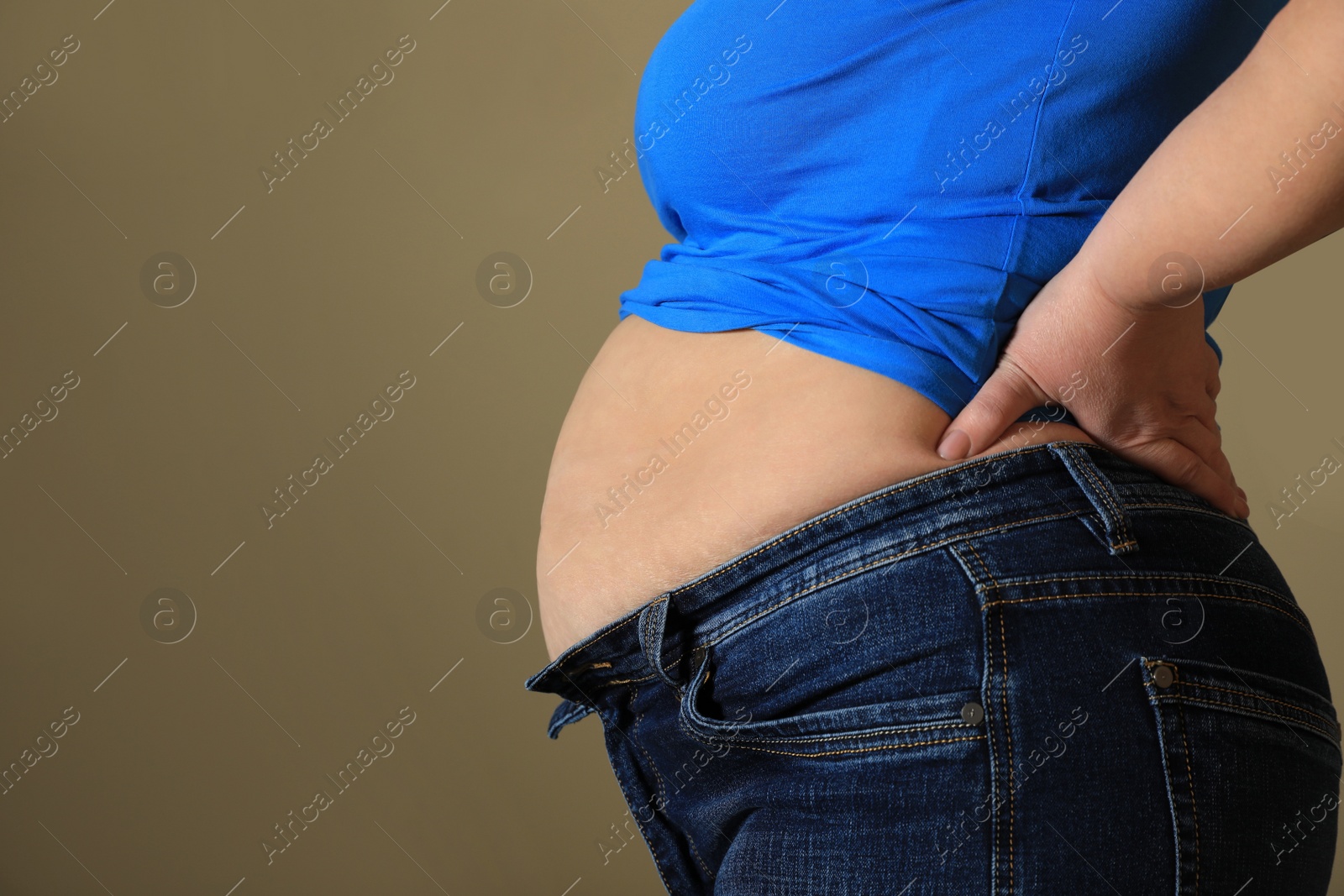 Photo of Overweight woman in tight shirt and jeans on light brown background, closeup. Space for text