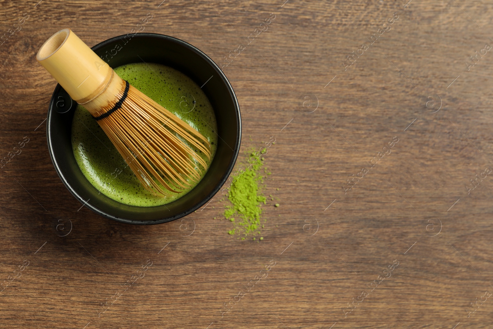 Photo of Cup of fresh matcha tea with bamboo whisk and green powder on wooden table, top view. Space for text