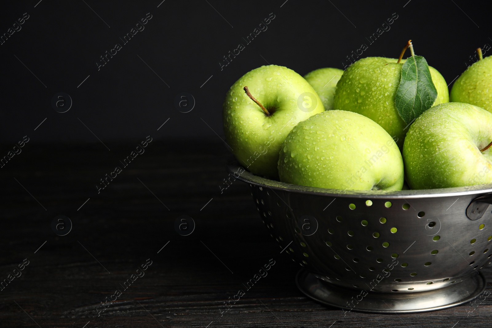 Photo of Colander of fresh ripe green apples on black wooden table, space for text