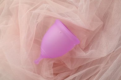 Photo of Menstrual cup on pink fabric, top view