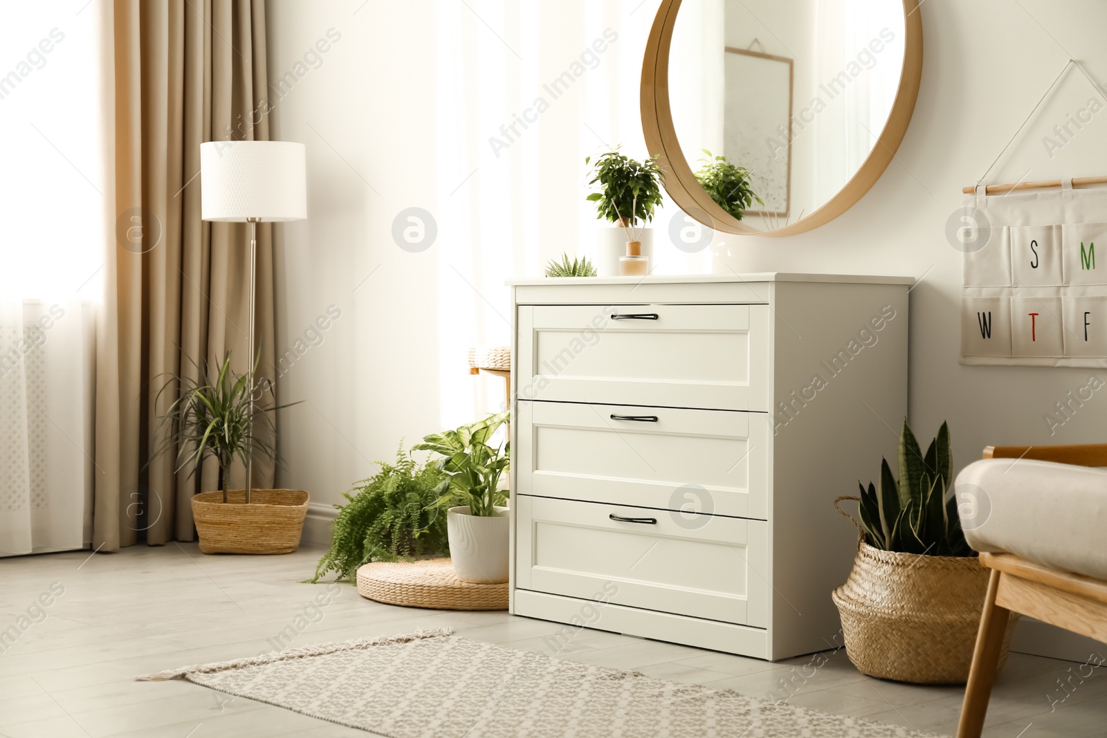 Photo of Stylish room interior with chest of drawers and round mirror