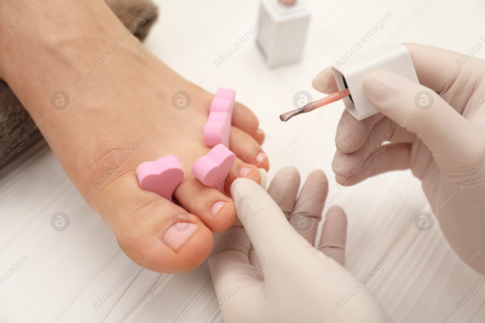 Photo of Professional pedicurist painting client`s toenails with polish in beauty salon, closeup