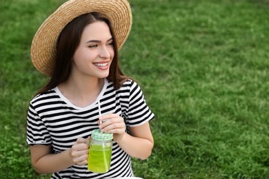 Photo of Young woman in straw hat with mason jar of fresh juice on green grass, space for text