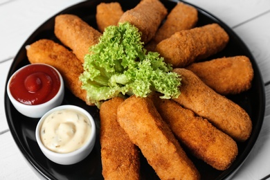 Photo of Plate of cheese sticks and sauces on table, closeup