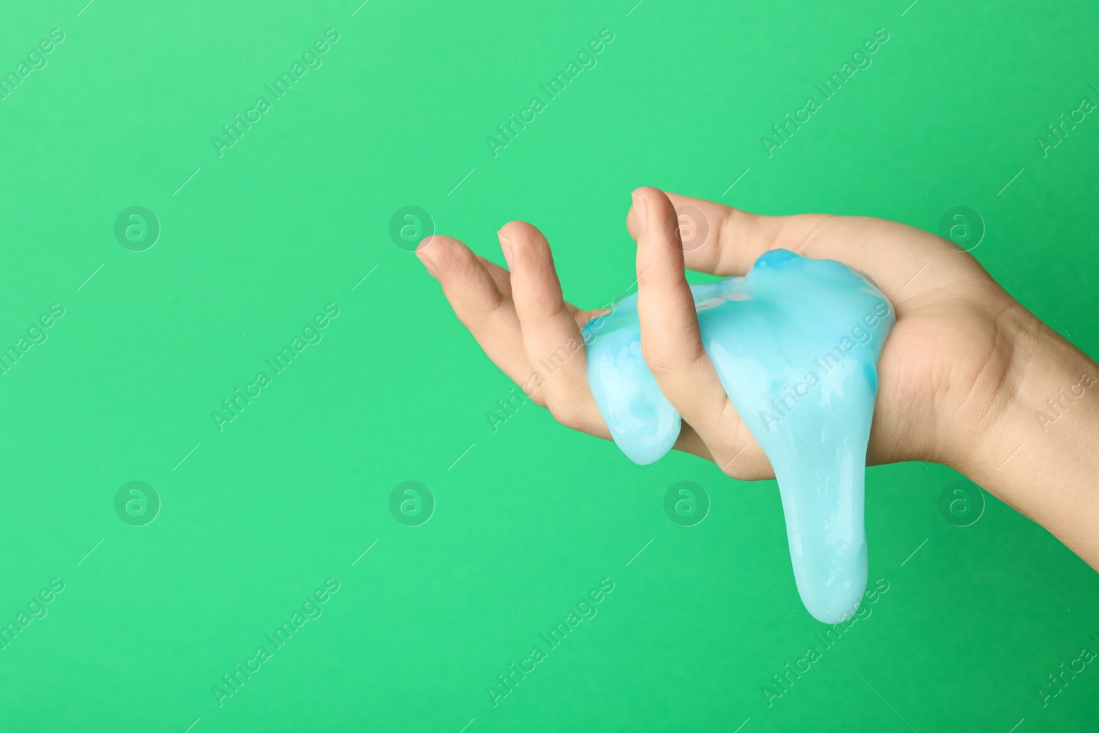 Photo of Woman playing with light blue slime on green background, closeup. Antistress toy