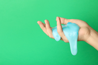 Woman playing with light blue slime on green background, closeup. Antistress toy