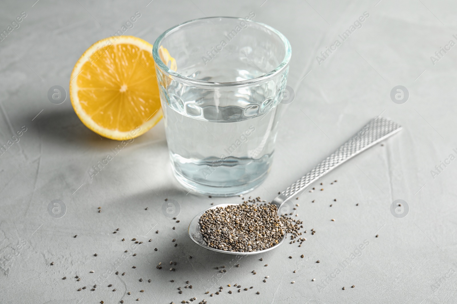 Photo of Spoon with chia seeds and glass of water on grey background