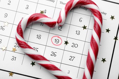 Photo of Saint Nicholas Day. Heart shape frame of candy canes and confetti on calendar with marked date December 19, flat lay