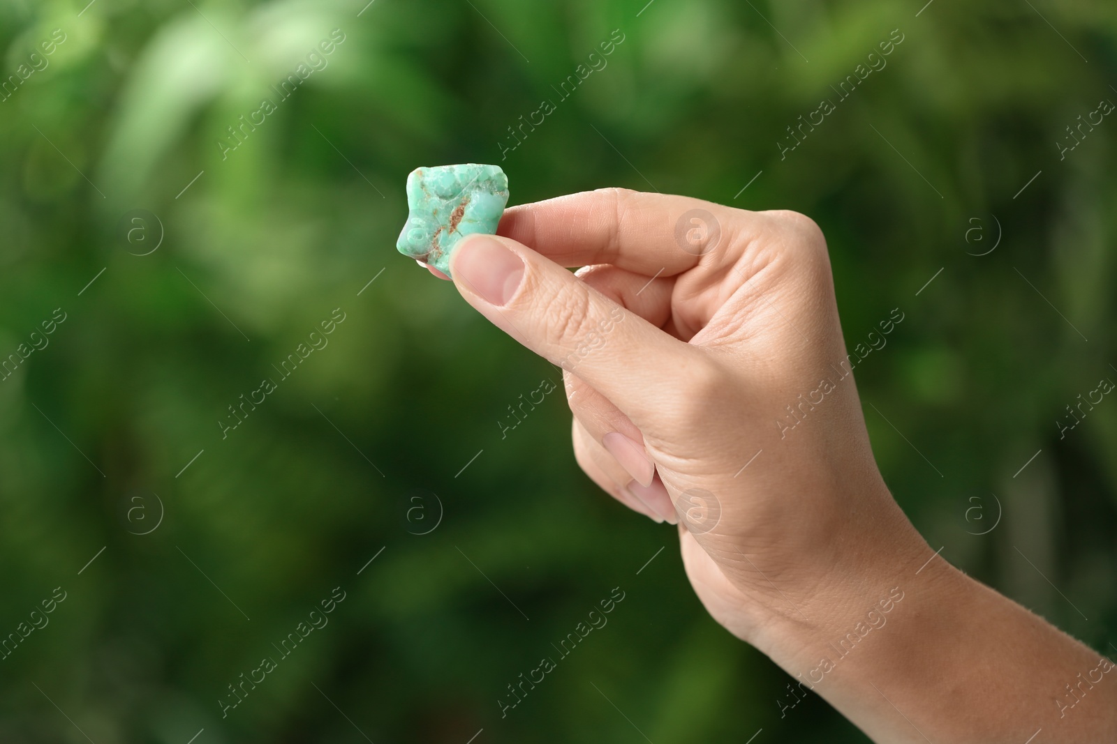 Photo of Woman holding beautiful chrysoprase gemstone on blurred green background, closeup