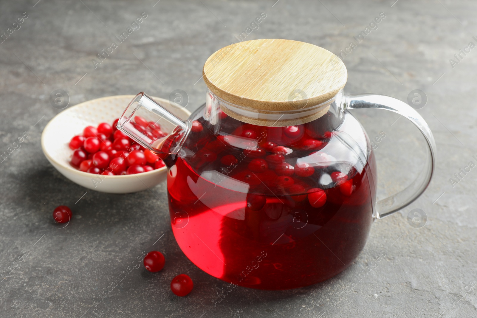 Photo of Tasty hot cranberry tea in teapot and fresh berries on light grey textured table