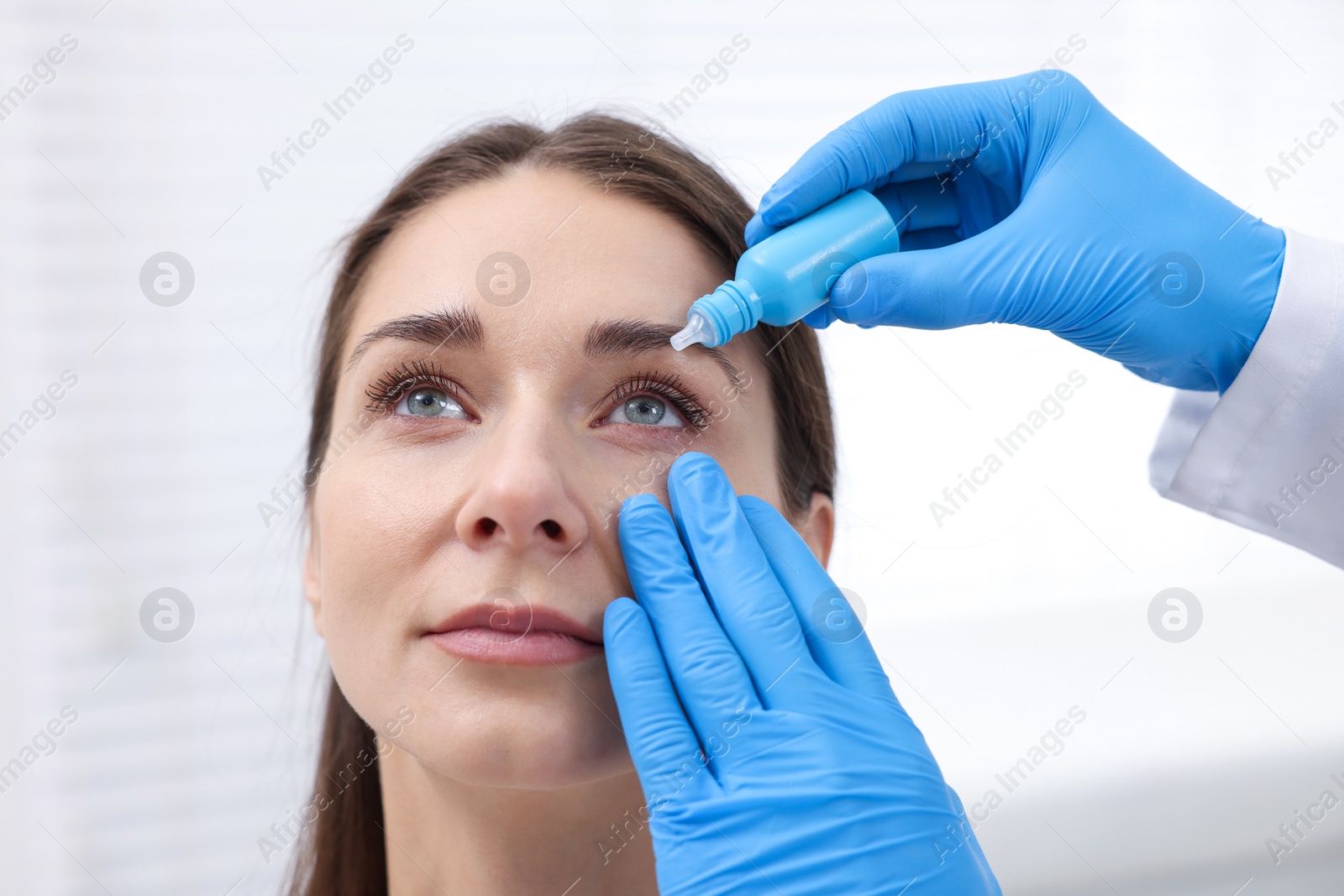 Photo of Doctor applying medical drops into woman's eye indoors