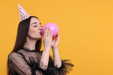 Photo of Woman in party hat inflating balloon on orange background, space for text