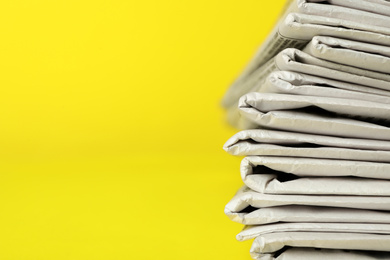 Stack of newspapers on yellow background, closeup with space for text. Journalist's work