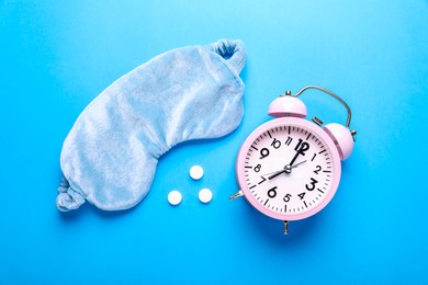 Photo of Soft sleep mask, pills and alarm clock on light blue background, flat lay