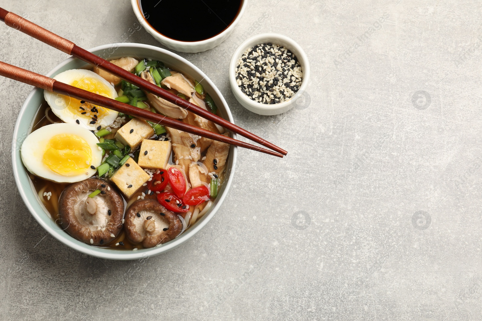 Photo of Delicious ramen served on grey table, flat lay with space for text. Noodle soup