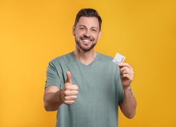 Photo of Happy man with condom showing thumb up on orange background
