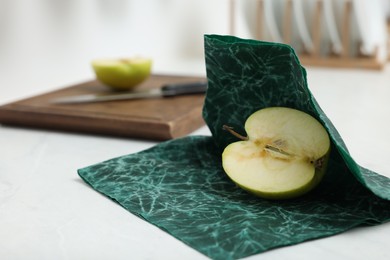 Half of apple with green beeswax food wrap on white table, closeup
