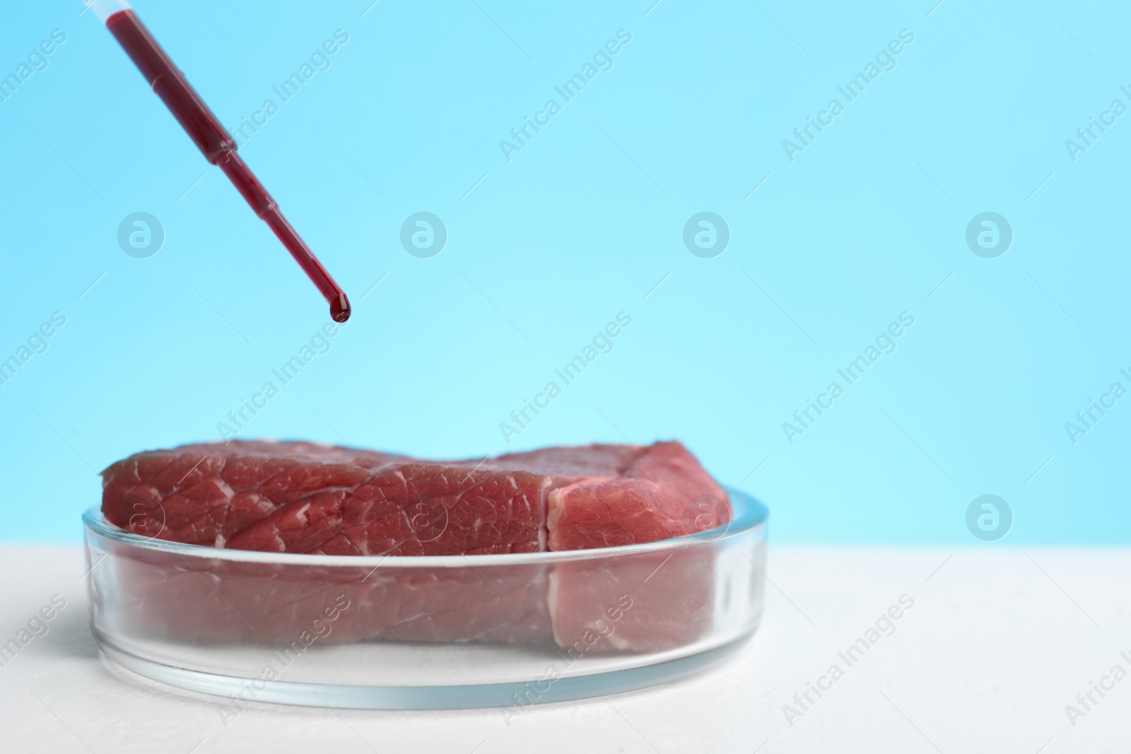 Photo of Dripping red liquid onto sample of lab grown meat on white table. Space for text