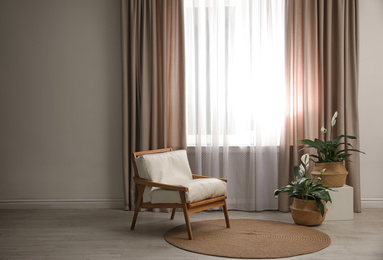 Comfortable armchair near window with elegant curtains in room