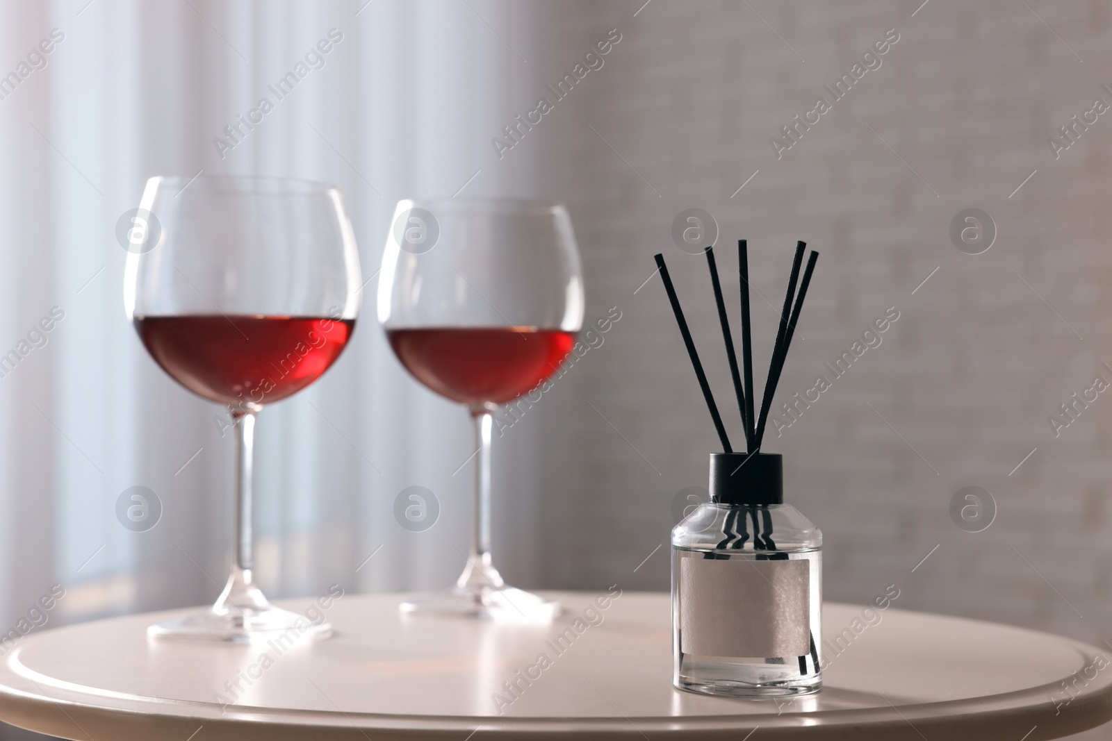 Photo of Reed diffuser and glasses of wine on white table indoors. Space for text