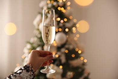 Woman with glass of champagne near Christmas tree at home, closeup. Space for text