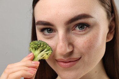 Photo of Beautiful woman making fake freckles with broccoli and cosmetic product on grey background, closeup