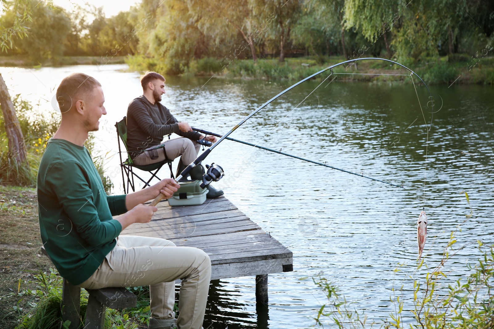 Photo of Friends fishing on wooden pier at riverside. Recreational activity