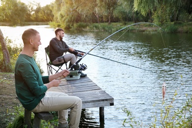 Photo of Friends fishing on wooden pier at riverside. Recreational activity