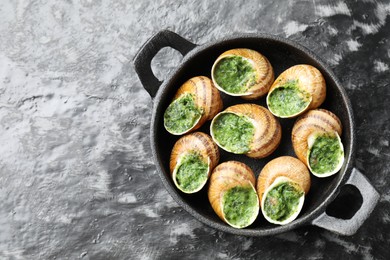 Photo of Delicious cooked snails in baking dish on grey textured table, top view. Space for text