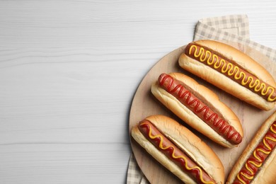 Photo of Fresh delicious hot dogs with sauces on white wooden table, top view. Space for text