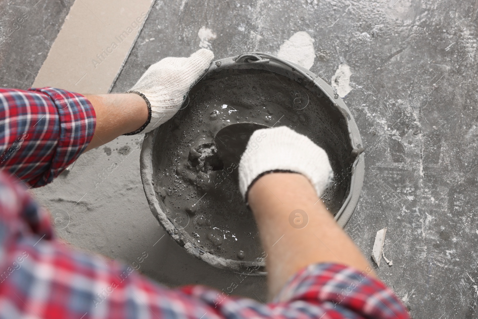 Photo of Worker with trowel mixing concrete in bucket indoors, closeup