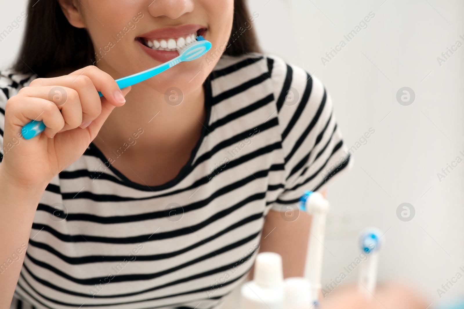 Photo of Woman brushing her teeth with plastic toothbrush near mirror in bathroom, closeup