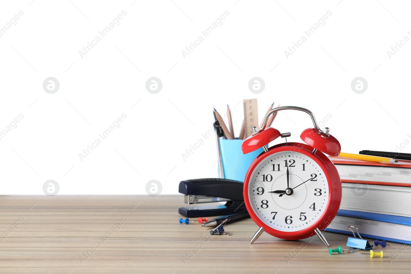 Photo of Red alarm clock and different stationery on wooden table against white background, space for text. School time