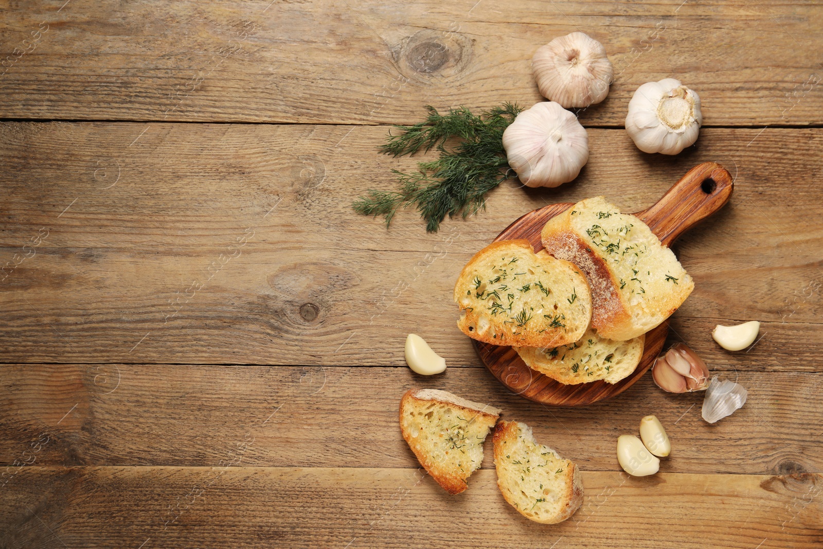 Photo of Tasty baguette with garlic and dill on wooden table, flat lay. Space for text