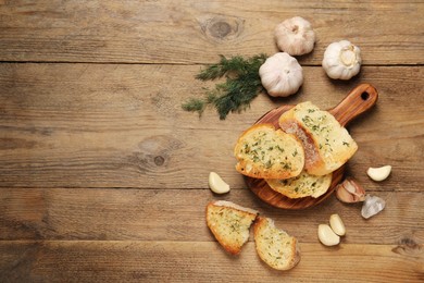 Tasty baguette with garlic and dill on wooden table, flat lay. Space for text
