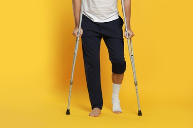 Photo of Man with injured leg using crutches on yellow background, closeup