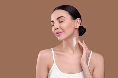 Photo of Beautiful woman with smear of body cream on her neck against light brown background. Space for text