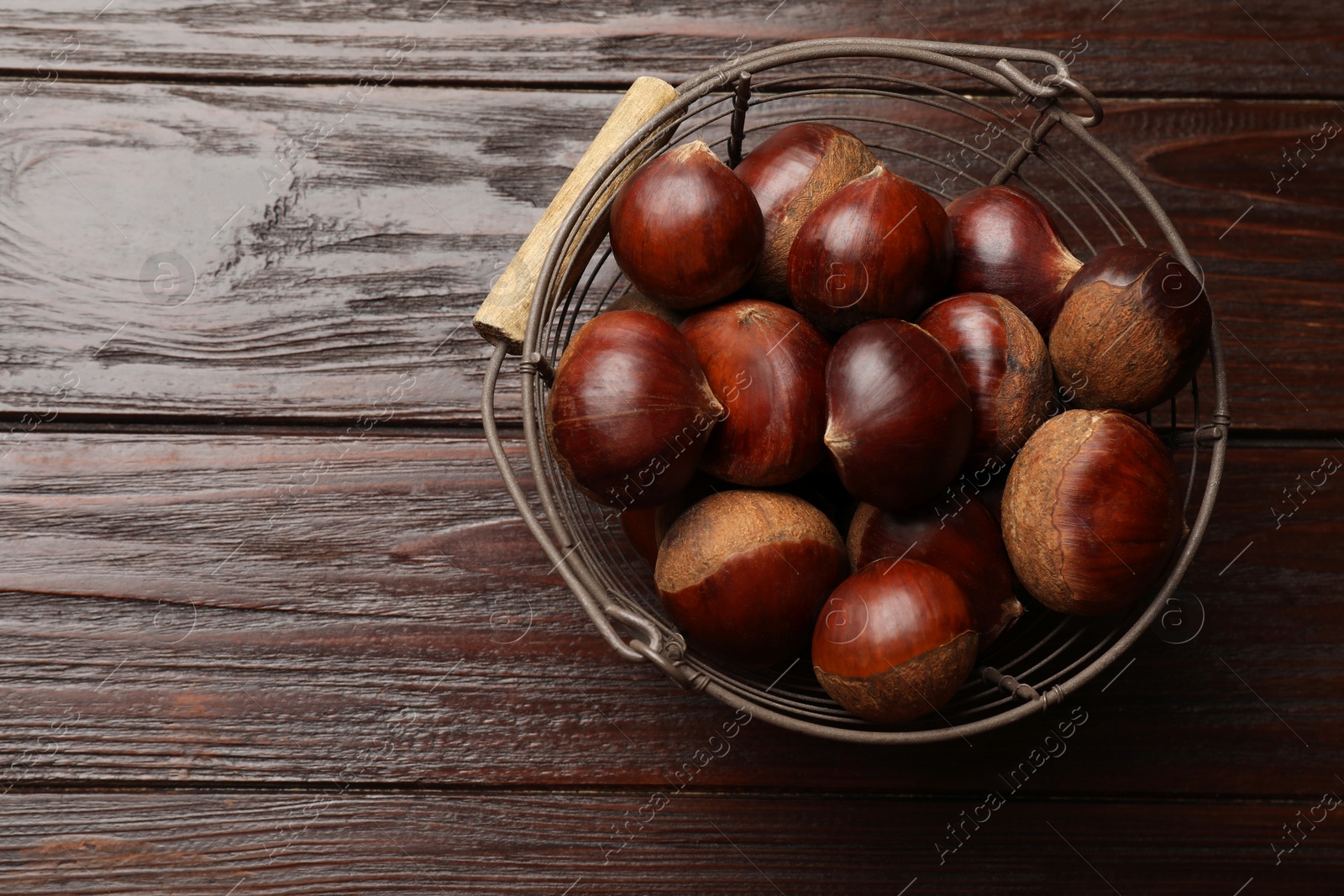 Photo of Sweet fresh edible chestnuts in metal basket on wooden table, top view. Space for text