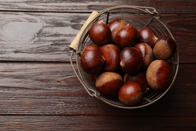 Sweet fresh edible chestnuts in metal basket on wooden table, top view. Space for text