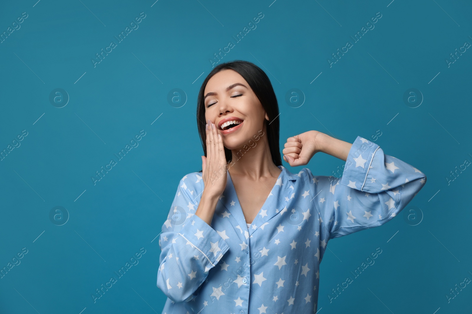 Photo of Beautiful Asian woman in pajamas yawning on blue background. Bedtime