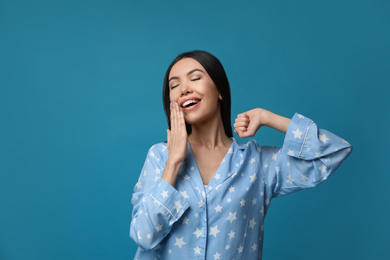 Photo of Beautiful Asian woman in pajamas yawning on blue background. Bedtime