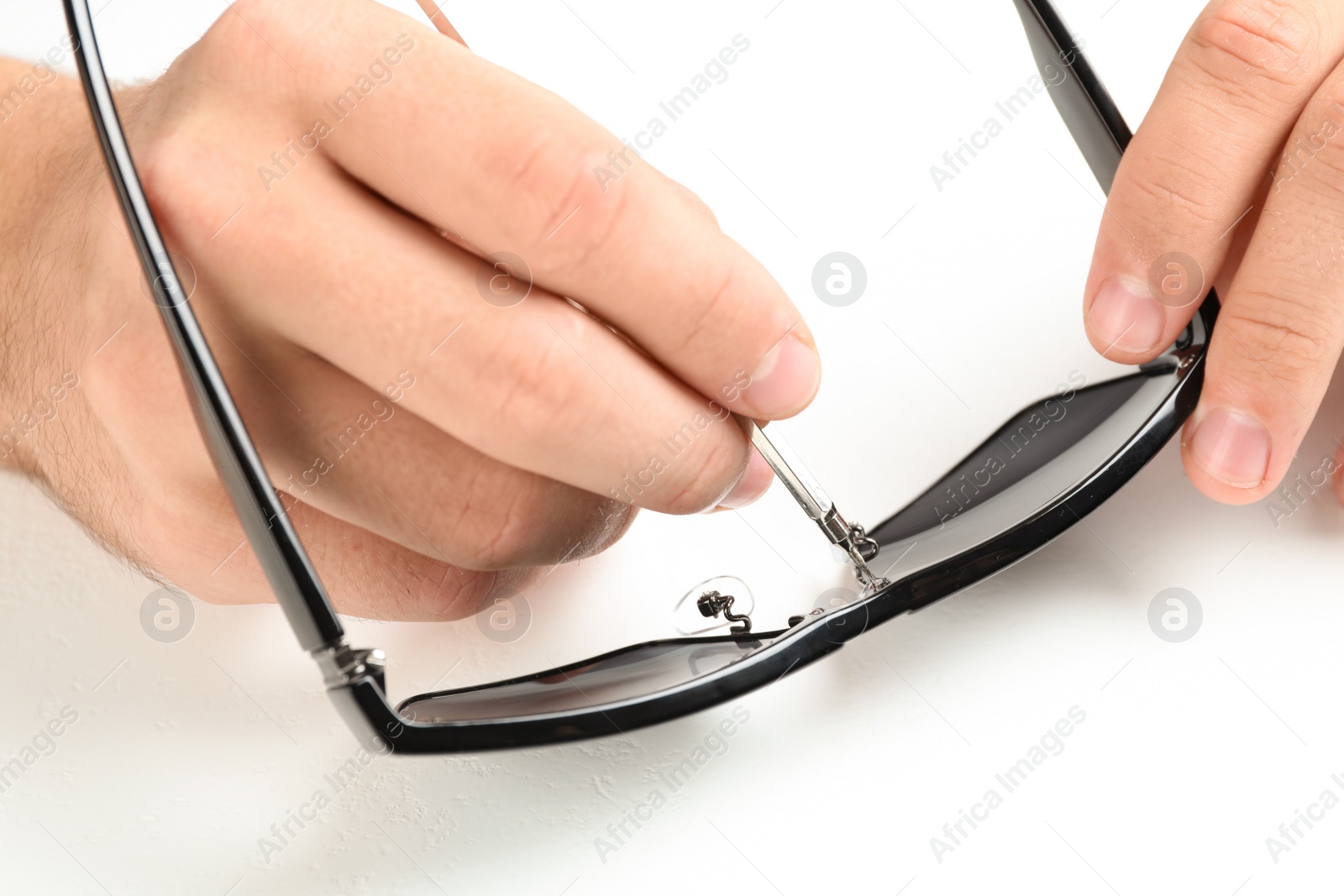 Photo of Handyman repairing sunglasses with screwdriver on white background, closeup