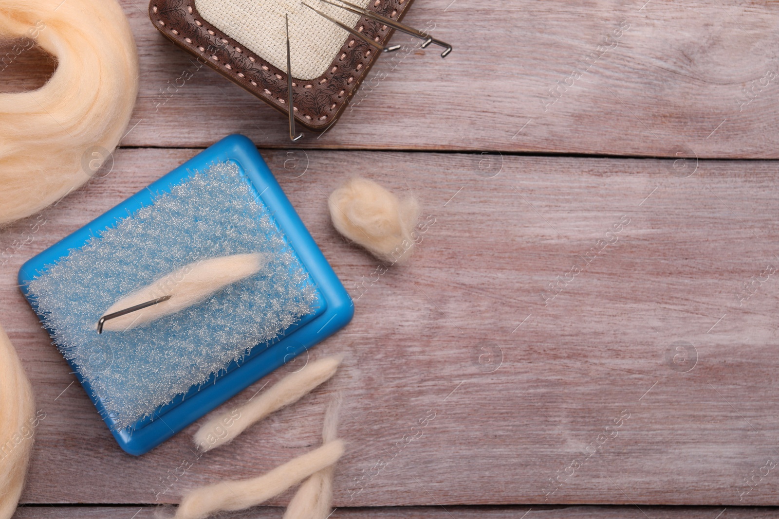 Photo of Felting tools and wool on wooden table, flat lay. Space for text