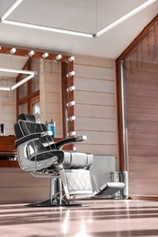 Stylish hairdresser's workplace with professional armchair and large mirror in barbershop, low angle view. Interior design