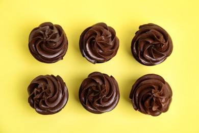 Photo of Delicious chocolate cupcakes with cream on yellow background, flat lay