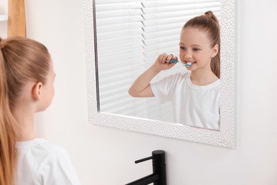 Cute little girl brushing her teeth with plastic toothbrush near mirror in bathroom