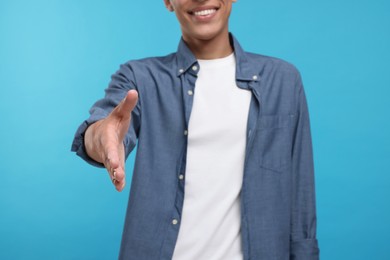 Photo of Happy man welcoming and offering handshake on light blue background, selective focus