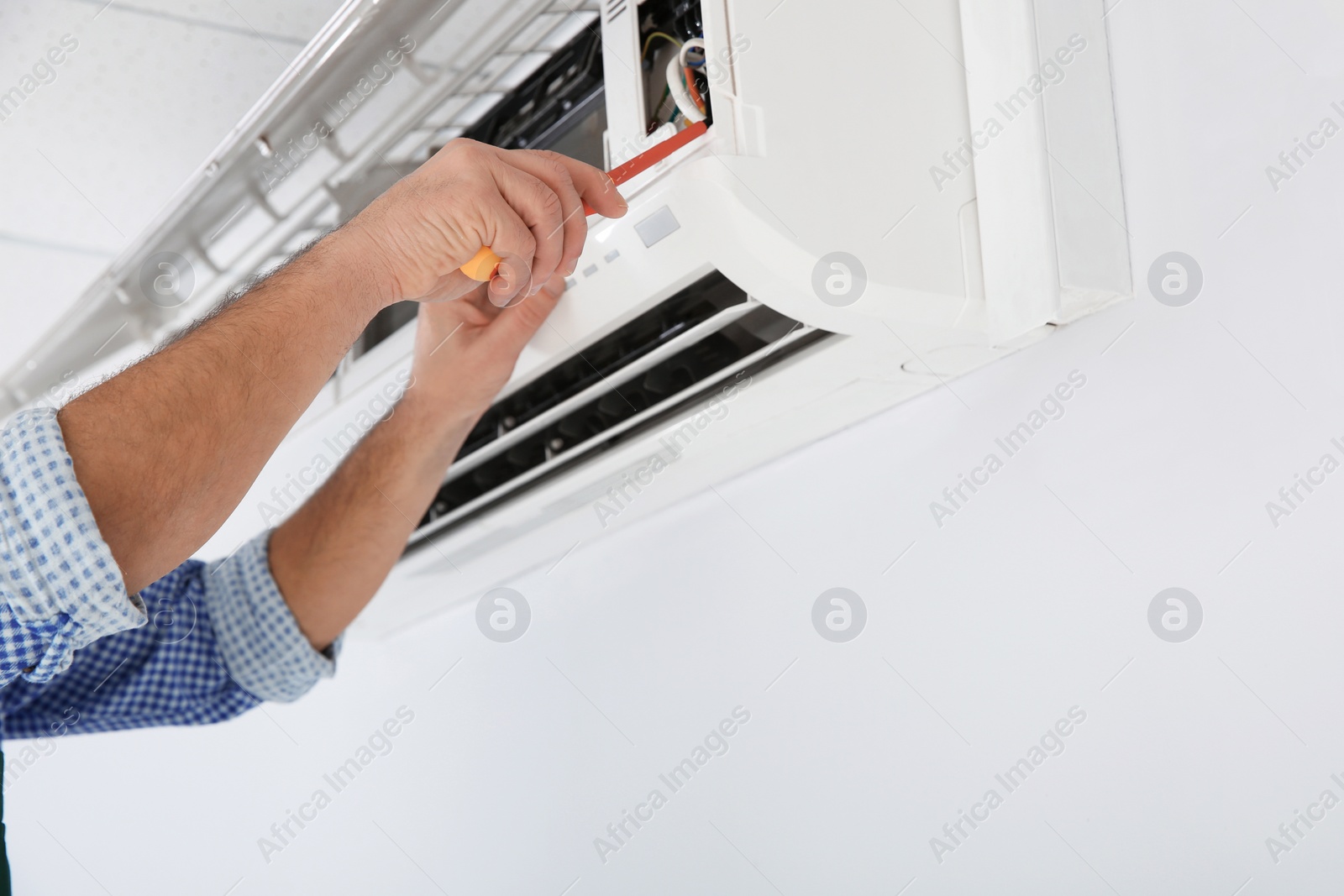 Photo of Electrician with screwdriver repairing air conditioner indoors, closeup