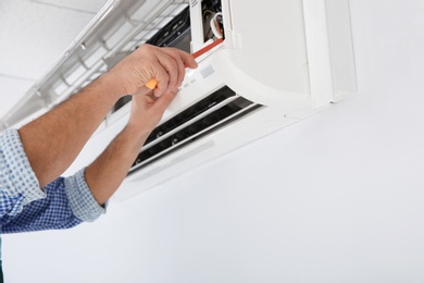 Electrician with screwdriver repairing air conditioner indoors, closeup