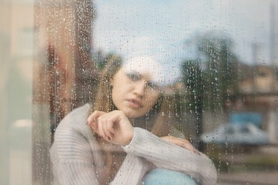 Photo of Depressed young woman near window, view from outside